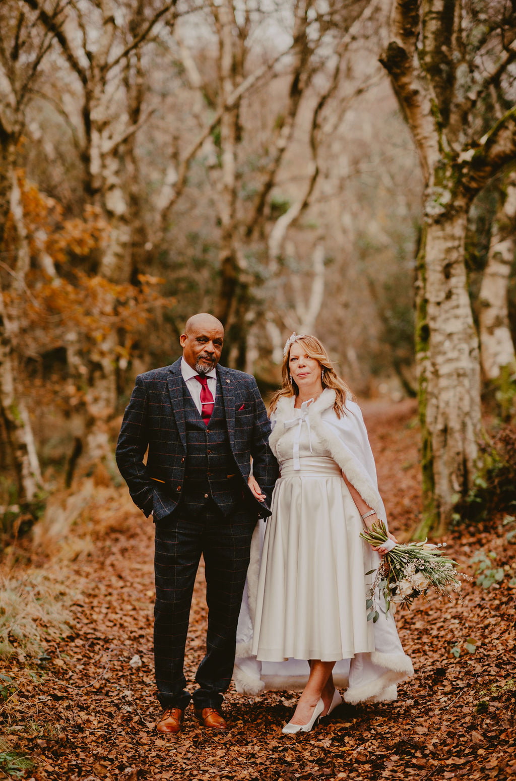 man and woman stood in the woods holding a wedding bouquet